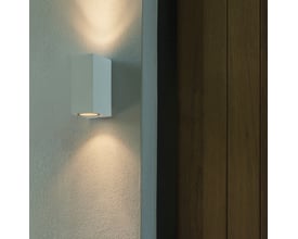 Astro Chios 150 SPA vægarmatur i hvid aluminium, monteret på en pudset væg ved siden af en træbeklædt væg, lyser opad og nedad.