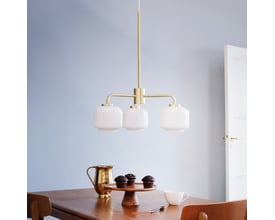 Dyberg Larsen Arp lysekrone med 3 opal glas og messing ophæng, vist over et træbord med muffins og kande.