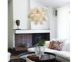 By Rydéns Gross Grande lysekrone monteret i en moderne stue med hvid sofa og en pejs, diameter 62 cm med ravglaskugler.