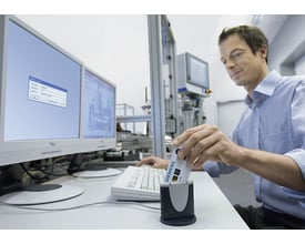 Siemens SIMATIC PCS7 seriel chipkortlæser i brug, med en mand der indsætter et kort og ser på en computerskærm med login-vindue.