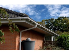 Plastmo tagrende monteret på en rød murstensbygning med grønne træer i baggrunden og en blå himmel.