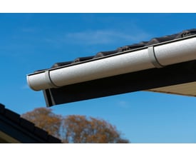 Plastmo tagrende i aluzink med en bredde på 120 mm, monteret på et mørkt hus med grå tagsten.