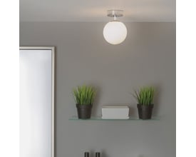 Astro 0323 Denver loftlampe i krom med opal glas, monteret på en grå væg over en glasreol med dekorationer.