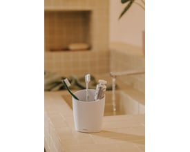 Cosmic Saku tandkrus i mat hvid med tandbørster og tandpasta sat i, placeret på en lys flisebelagt bordplade.