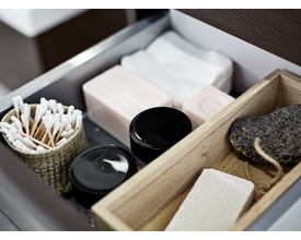 Dansani skuffeindsats i eg med vatpinde, sæber og pimpsten, viser praktisk opbevaring i et badeværelse.