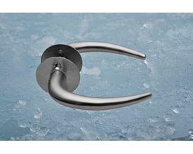 Assa Abloy Coupe-dørgreb i børstet rustfrit stål, vist skråt med slanke, buede greb og runde beslag.