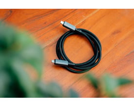 Sort Verbatim Sync & Charge USB-C-kabel, USB4 med 240 W opladning og 40 Gbit/s, ligger oprullet på et træbord.