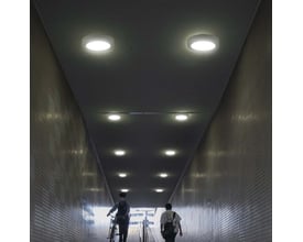 V-TAC rund LED-loftslampe på 12 W med hvid kant lyser i loftet i en lang, flisebelagt passage.