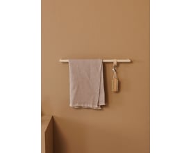 Metallbude Vana håndklædestang i creme med et lyst håndklæde og en børste, vist på en mørkere beige væg.