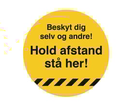 Gulvskilt med teksten "Beskyt dig selv og andre! Hold afstand stå her!" i gul med sorte detaljer. 33cm diameter.