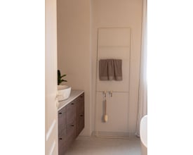 Metallbude Estina håndklædestige i beige, 1800mm høj, med et håndklæde hængende på den. Stigen står ved siden af et badeværelsesmøbel med vask.