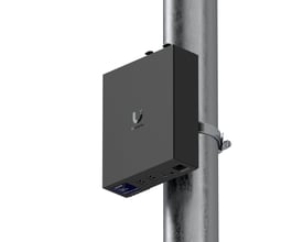 Ubiquiti Enterprise Audio/Video Bridge, en sort AV-bro monteret på en mast med logo og tilslutninger synlige.