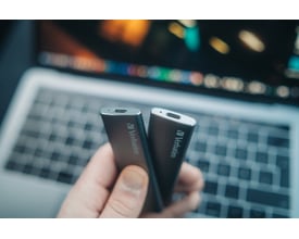 To Verbatim VX500 eksterne SSD-enheder holdes foran en bærbar, så deres kompakte kabinetter og stik ses.