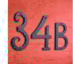Smedbo husnummer 34B i sort smedejern, monteret på en tekstureret, orangerød facade, der viser nummerets klassiske design og mørke finish.