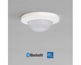 Niko P41LR tilstedeværelsessensor til indbygning i hvidt, monteret på et gråt loft med Bluetooth og IEC logoer nederst.