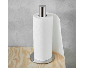 Bastant Design køkkenrulleholder i poleret rustfrit stål med en køkkenrulle monteret, placeret på en træhylde foran en grå væg.