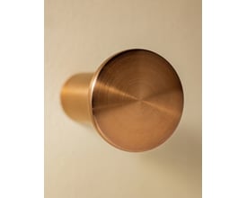 Top view af Cosmic Hook i børstet kobber, med synlig børstet finish og en skygge på den beige væg.