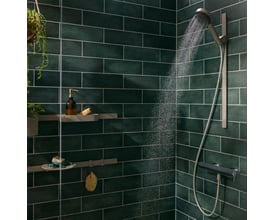 Brusekabine med Hansgrohe opbevaringskurv, brusehoved og en brusebadsarmatur på en mørkegrøn flisevæg.