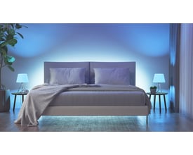 Nanoleaf Essentials Matter Smart Bulb E27 skaber stemningsfuld blå belysning i et soveværelse med dobbeltseng og sengeborde.