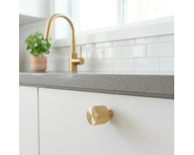 Beslagsboden knop i børstet messing, Ø22 mm, monteret på en hvid skuffe i et lyst køkken.