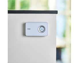 Monteret Foss Europe TREND dørklokke i hvid på en lys væg med en sort kant øverst, baggrund med grønne nuancer.