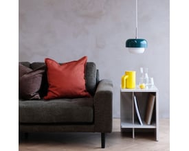 Dyberg Larsen HAIPOT pendel i mørkegrøn og hvid, hængende over et sidebord ved siden af en grå sofa, i en moderne stueindretning.