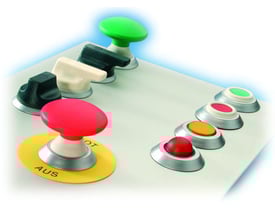 Oversigt over forskellige trykknapper og drejeknapper monteret på en kontrolpaneloverflade, herunder rød STOP-knap og grøn lys-knap.