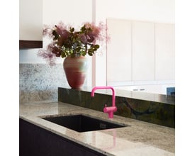 Elegant Vola KV1 køkkenarmatur i pink messing integreret i et moderne køkkenmiljø ved siden af en sort vask og et stort blomsterarrangement.