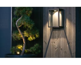 SG Armaturen Fagernes Mini væglampe i sort aluminium med 2700K lys, monteret på trævæg og lyser indirekte.