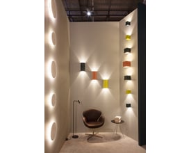 Forskellige Astro vægarmaturer i gips udstillet på en væg, med en stol og et lille bord i forgrunden.