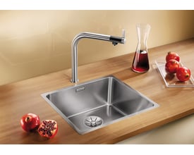 Blanco Andano 450-IF/N UXI køkkenvask i rustfrit stål på en træbordplade med et højt armatur, granatæbler og en karaffel med rød væske.