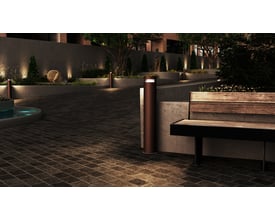 Ansell Lighting Avio pullert med sort halvskærm oplyser en udendørs terrasse med fliser og bænk om aftenen.