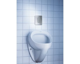Grohe Skate Cosmopolitan urinal betjeningsplade i matkrom monteret på en lyseblå flisevæg ved siden af et hvidt urinal.