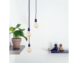 Nielsen Light Klyngependel K9 med 3 sorte tekstilledninger og dekorative pærer, monteret på væggen ved siden af en plante og fuglefigurer.