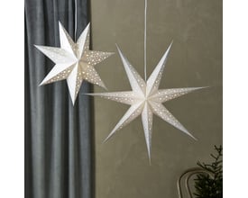 To Markslöjd blanke pendel stjerner i sølv, 75 cm, hængende indendørs i et rum med gardiner og en gren, der skaber julestemning.