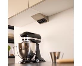 Loevschall dobbelt stikkontakt i ståltrekant design monteret under et køkkenskab med en køkkenmaskine i forgrunden.