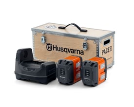 Husqvarna PACE power kit med B750X batteri og C1800X oplader, præsenteret foran en trækasse med Husqvarna logo.