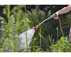 Bruger vander blomster i haven med Gardena Classic lang brusepistol, der afgiver en bred vandstråle.