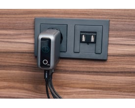 Verbatim mini GaN-oplader på 140 W sidder i en stikkontakt med displayet vendt frem og kabler tilsluttet.