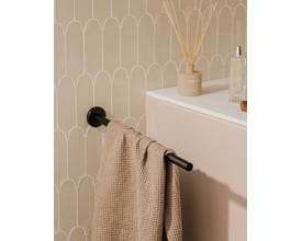 Cosmic håndklædeholder i mat sort med en lys beige vaffelhåndklæde hængende. Holderen sidder op ad en væg med beige buede fliser.