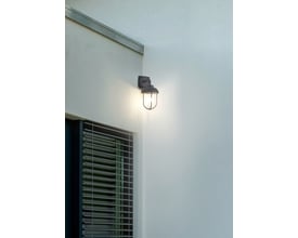 Trio Lighting hjørnefæste med en tændt udendørs væglampe, placeret på et hjørne ved et vindue med persienner.