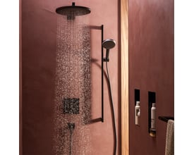 Hansgrohe Raindance Alive S håndbruser i mat sort, vist i brug med brusehoved, der sender PowderRain stråler mod en rustik væg.