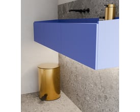 Unidrain Reframe pedalspand i messing placeret på et moderne badeværelsesgulv ved siden af et blåt vægskab.