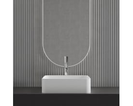 Scandtap Voyage High Classic håndvaskbatteri med blank stålfinish monteret på en hvid, rektangulær håndvask foran en dekorativ, grå ribbet væg.