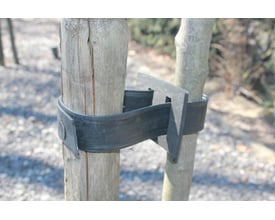 GreenMax gummiklods fastgjort mellem to træstammer med en sort gummirem og metalplader, ideel til stabilisering.