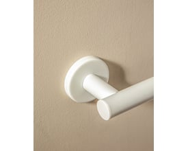 Nærbillede af den matte hvide vægbeslag på Cosmic toiletpapirholderen, som er monteret på en beige væg.