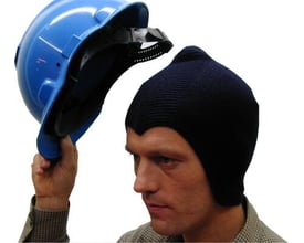 En mand tager en blå strikket hjelmhue under en blå sikkerhedshjelm på en hvid baggrund.