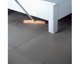 Svedbergs badekar 1204, 1400x700 mm, hvid, bliver rengjort med en kost på et gråt flise gulv.