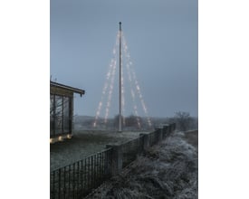 Konstsmide flagstangskæde med 500 lys, installeret på en flagstang i tåget vejr, med et hus i baggrunden.