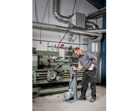 Fein GRIT GKS 75 kompakt-båndsliber i brug i et værksted med en mand, der arbejder på metal og gnister flyver.
